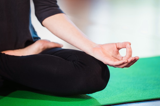 Joga dziewczyna medytuje wewnątrz i robi zen symbolowi jej ręką. Zbliżenie kobiety ciało w joga pozie na zielonej macie