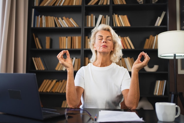 Zdjęcie joga, uważność, medytacja, brak stresu, zachowanie spokoju, kobieta w średnim wieku, praktykująca jogę w biurze.