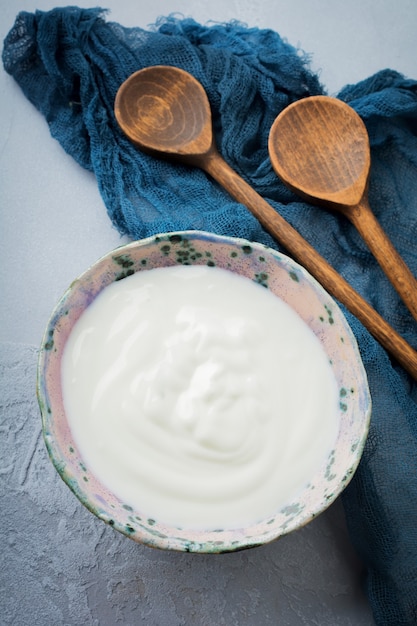 Jogurt grecki w talerzu ceramicznym z drewnianymi łyżkami na szarym tle betonu Styl rustykalny.