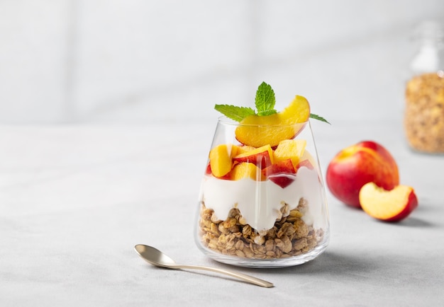 Jogurt parfait z brzoskwinią i granolą w kieliszku na jasnym tle z świeżymi owocami Koncepcja zdrowego odżywiania