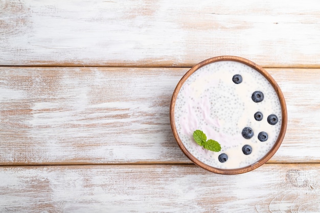 Jogurt z jagodami w drewnianej misce na białej powierzchni drewnianej