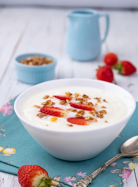 Jogurt z truskawkami i muesli w misce nad białym drewnianym stołem