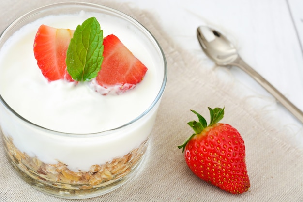 Jogurt z zbożami i truskawkami na białym drewnianym stole