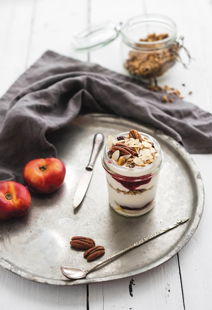 Jogurtowa granola owsiana z jagodami miodowymi orzechami i nektarynami w szklanym słoju na vintage metalowej tacy na rustykalnym białym tle