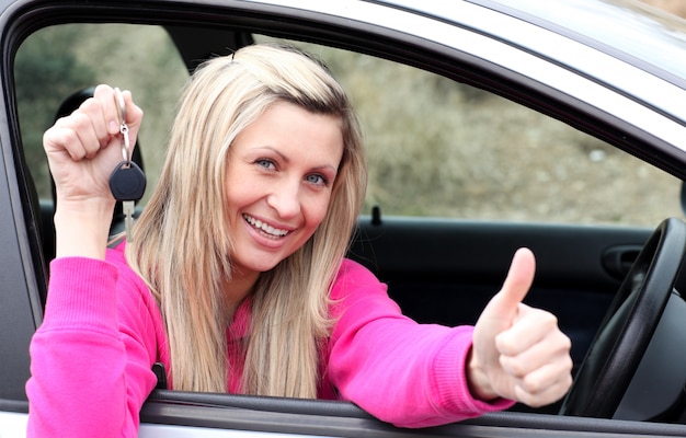 Jolly żeński kierowca pokazujący klucz po przejściu nowego samochodu