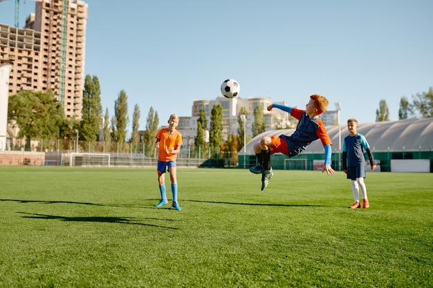 Zdjęcie junior skacze do przodu, aby kopnąć piłkę nogą biorącą udział w meczu piłki nożnej. szkolna gra sportowa w piłce nożnej