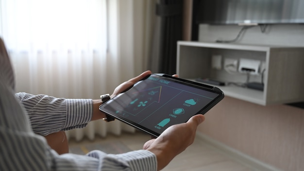 Kadrowane dłonie obrazu używają tabletu z aplikacjami sterowanymi przez urządzenia domowe na ekranie.
