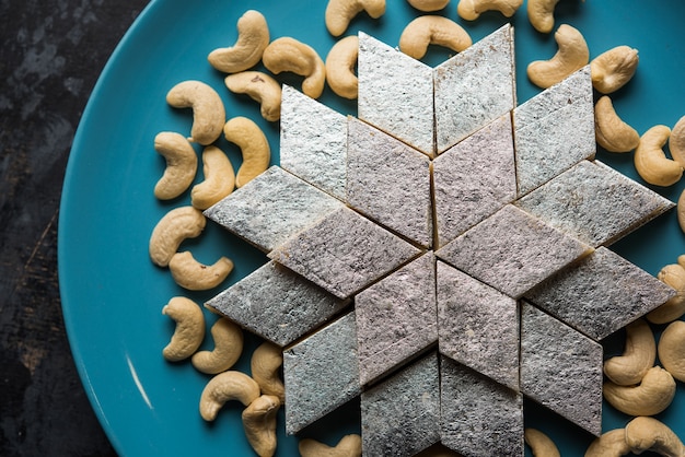 Kaju Katli to indyjskie słodycze w kształcie rombu wykonane z cukru nerkowca i mava, podawane w talerzu na nastrojowej powierzchni. selektywne skupienie