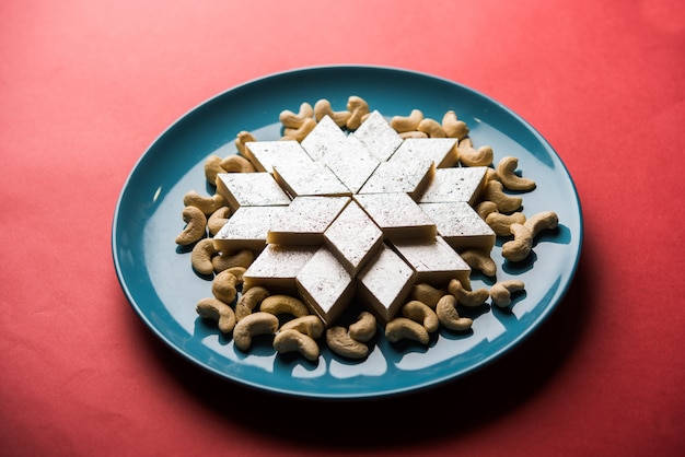 Kaju Katli to indyjskie słodycze w kształcie rombu wykonane z cukru nerkowca i mava, podawane w talerzu na nastrojowej powierzchni. selektywne skupienie
