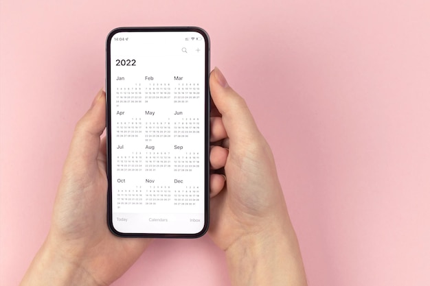 Kalendarz 2022. Smartfon w rękach kobiety. Różowe tło, obszar roboczy, do zrobienia, zdjęcie koncepcji planowania nowego roku
