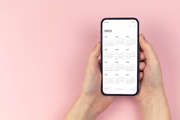 Kalendarz 2022. Smartfon w rękach kobiety. Różowe tło, obszar roboczy, do zrobienia, zdjęcie koncepcji planowania nowego roku