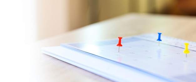 Zdjęcie kalendarz closeup czerwona szpilka na pustym biurku kalendarz z urządzeniami biurowymi