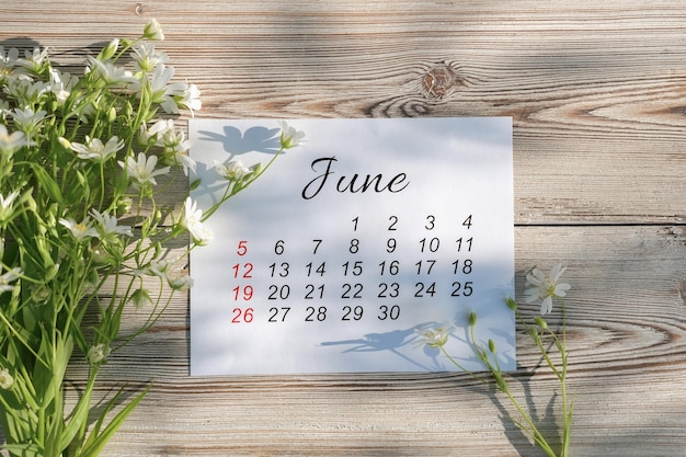 Kalendarz czerwiec 2022 i białe kwiaty na drewnianym tle