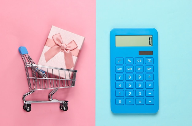 Kalkulator i wózek na zakupy z pudełkiem na różowo-niebieskim pastelu. Obliczenie wartości prezentu.