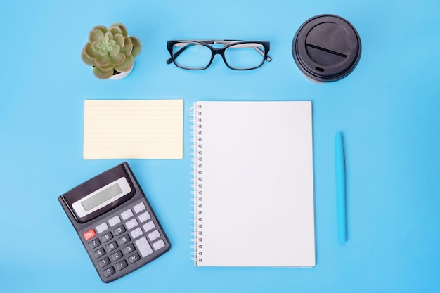 Kalkulator pusty papier notatkowy kawałek papieru szklanki do kawy roślina i długopis na niebieskim tle miejsca pracy