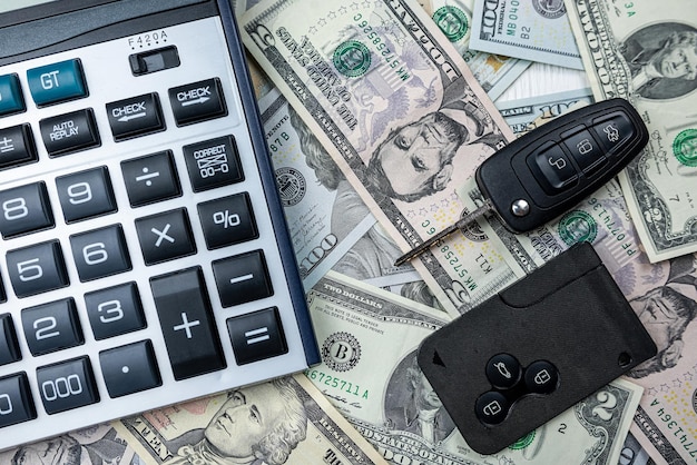 Kalkulator z dwoma czarnymi prawdziwymi kluczami do samochodu nad dolarami amerykańskimi jako tło Leasing lub zakup samochodu