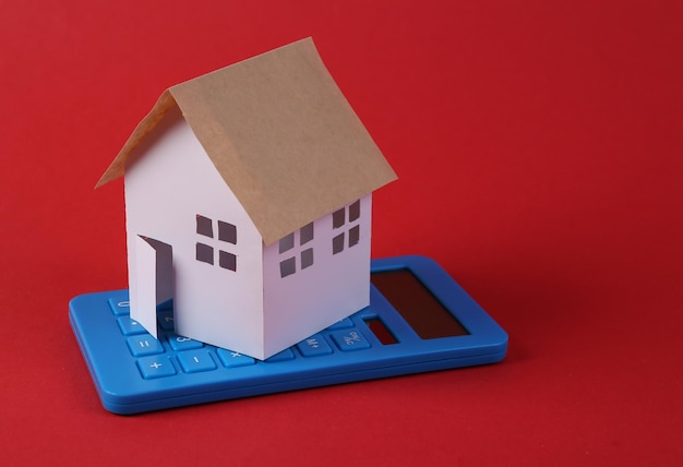 Kalkulator z małym modelowym domem na czerwonym tle Koncepcja oszczędności