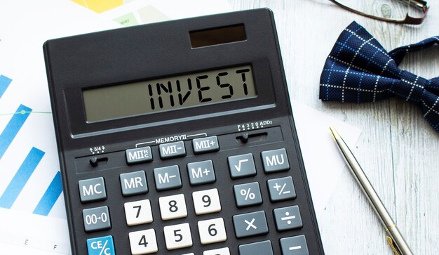 Kalkulator z napisem INVEST leży na dokumentach finansowych w biurze