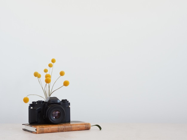 Kamera analogowa na antycznej książce z żółtym zaokrąglonym bukietem kwiatów z tyłu Na górze blatu z szarym tłem i przestrzenią do kopiowania