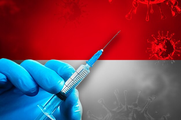 Kampania szczepień w Indonezji Covid19 Ręka w niebieskiej gumowej rękawiczce trzyma strzykawkę przed flagą