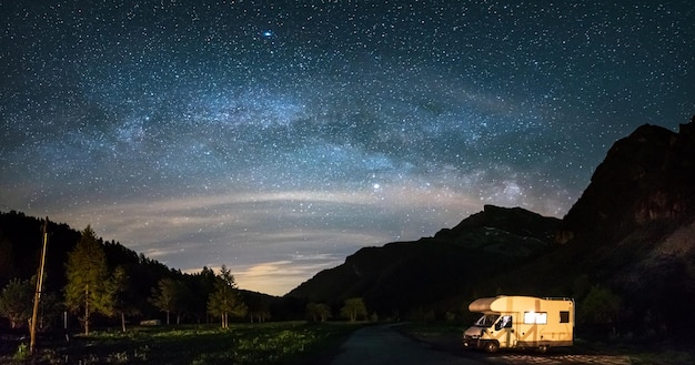 Kamper pod panoramicznym nocnym niebem w Alpach Galaktyka Drogi Mlecznej i gwiazdy nad oświetlonym kamperem Wolność na kempingu w wyjątkowym krajobrazie