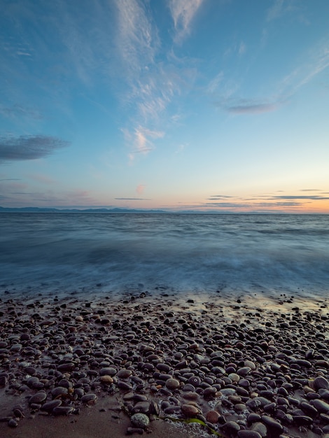 Zdjęcie kamyki wzdłuż plaży z falami i niesamowitym niebem.