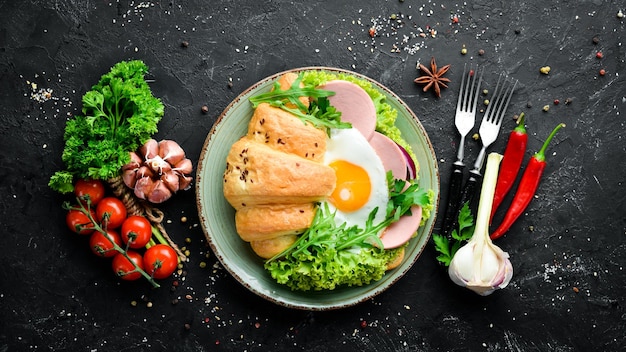 Kanapka Croissant z jajkiem sadzonym i kiełbaskami z pomidorami i cebulą Widok z góry Wolne miejsce na tekst