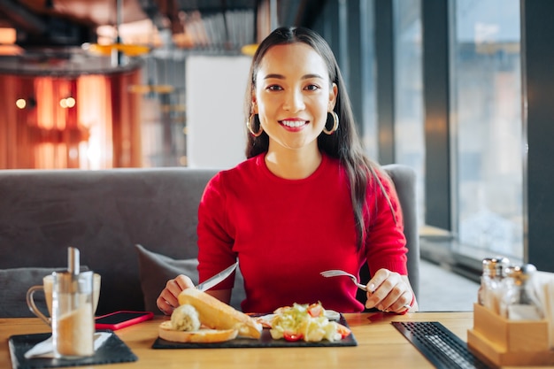 Kanapka i sałatka. Ciemnooka piękna kobieta je pyszną kanapkę i sałatkę w restauracji