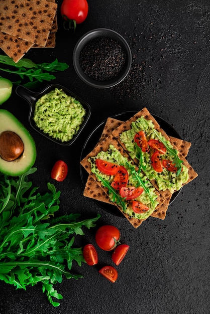 Kanapka z awokado z kremem z awokado i żytnim pieczywem chrupkim na przekąskę. Błonnik, żywność fitness i dieta. Chleb żytni z guacamole, rukolą i pomidorkami cherry na ciemnym tle. Zdjęcie wysokiej jakości