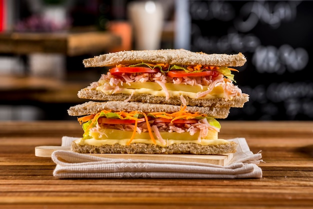 kanapka z chlebem, serem, marchewką, pomidorem i szynką na drewnianym stole