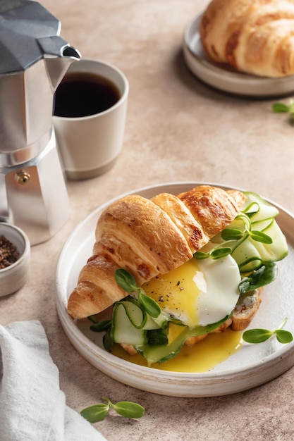 Zdjęcie kanapka z rogalikiem ze smażonym ogórkiem, serem jajecznym i mikro zieleniną oraz kawą na beżowym tle