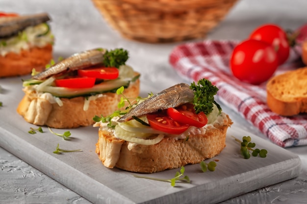 Kanapka ze szprotem wędzonym - ryba, świeży ogórek i pomidor. Kanapki ze szprotami na tostowych kromkach chleba