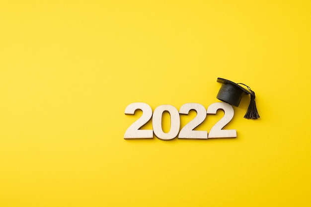 Kapelusz absolwenta z drewnianym numerem 2022 na żółtym tle. Edukacja, wychowanie, koncepcja klasy 2022