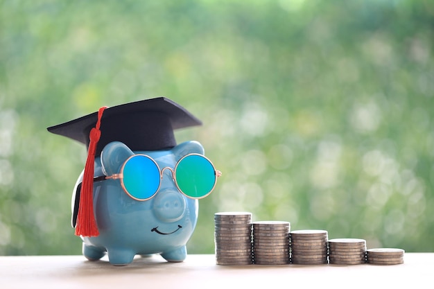 Zdjęcie kapelusz ukończenia szkoły na skarbonce ze stosem monet pieniędzy na naturalnym zielonym tle oszczędzanie pieniędzy na koncepcję edukacji