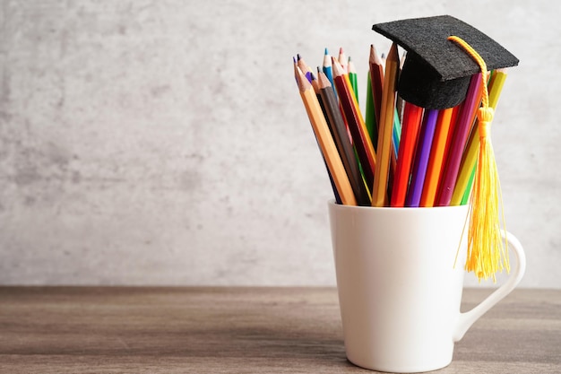 Kapelusz ukończenia szkoły z kolorowymi ołówkami na książce z kopią przestrzeni uczenia się koncepcji edukacji uniwersyteckiej