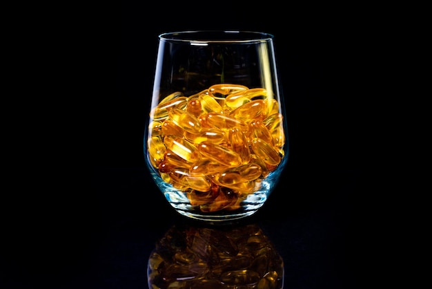 Kapsułki oleju rybiego Żółte tabletki omega 3 w słoiku na ciemnych czarnych kapsułkach oleju rybnego w kieliszku do wina w słoiku w wiadrze ampułki