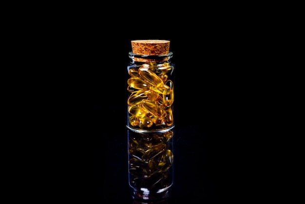 Kapsułki oleju rybiego Żółte tabletki omega 3 w słoiku na ciemnych czarnych kapsułkach oleju rybnego w kieliszku do wina w słoiku w wiadrze ampułki