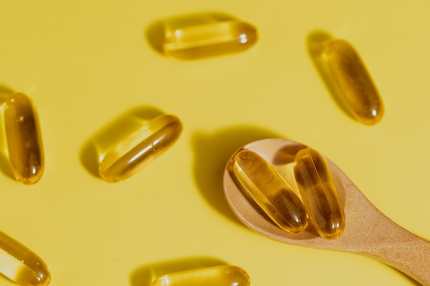 Kapsułki oleju rybnego Omega-3 w drewnianej łyżce na żółtym tle dla koncepcji opieki zdrowotnej