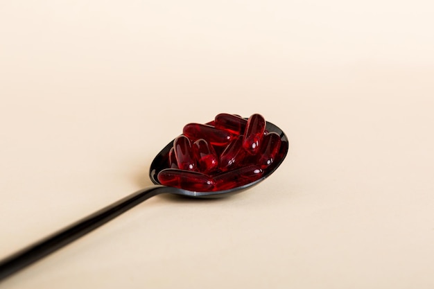 Kapsułki witaminowe w łyżce na kolorowym tle Tabletki podawane jako zdrowy posiłek Czerwone miękkie żelowe kapsułki witaminowe na łyżce