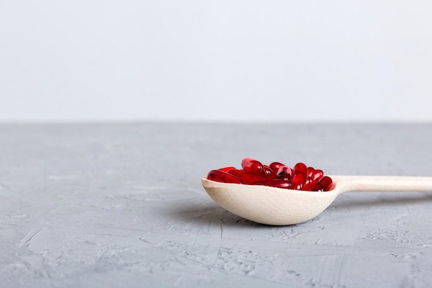 Kapsułki witaminowe w łyżce na kolorowym tle Tabletki podawane jako zdrowy posiłek Czerwone miękkie żelowe kapsułki witaminowe na łyżce