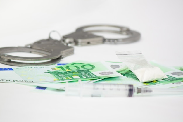 Karą Za Handel Narkotykami Jest Więzienie. Kajdanki Na Banknotach, Kokainie I Strzykawce Na Białym Tle Euro