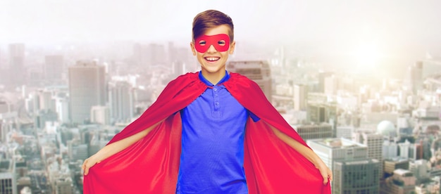karnawał, dzieciństwo, władza, gest i koncepcja ludzi - szczęśliwy chłopiec w czerwonej pelerynie superbohatera i masce na tle miasta