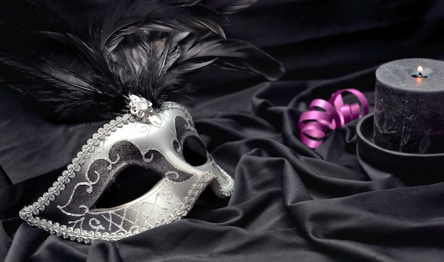 Karnawałowa maska na ciemnym satynowym materiale ze świecą i różową wstążką