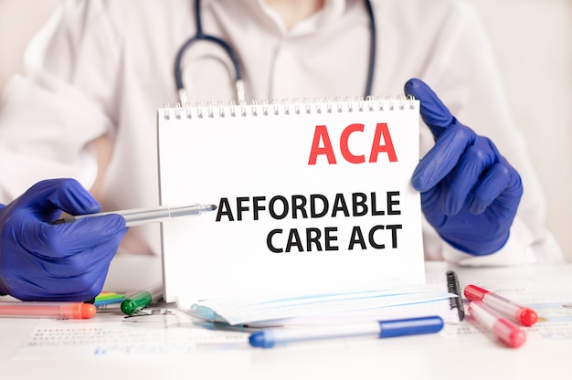 Karta Aca W Rękach Lekarza. Ręce Lekarza W Niebieskich Rękawiczkach Trzyma Kartkę Papieru Z Tekstem Aca - Skrót Od Affordable Care Act, Pojęcie Medyczne.