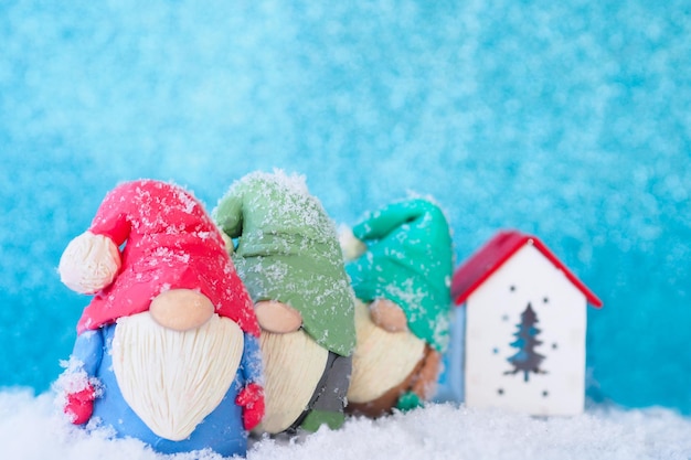 Kartka bożonarodzeniowa Trzy figurki śmiesznych krasnali, pokryte śniegiem, stoją jedna za drugą w pobliżu drewnianego domku.