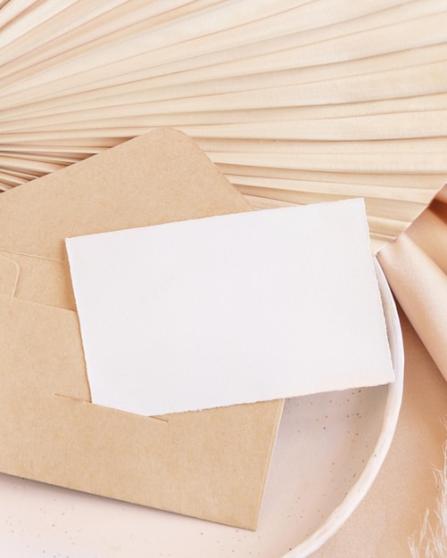 Kartka i koperta na talerzu na suszonym liściu palmowym i beżowej jedwabistej tkaninie z bliska powitanie lub makieta ślubna