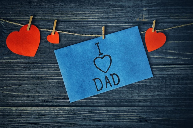 Zdjęcie kartka na dzień ojca i papierowe serca na sznurku na drewnianym tle