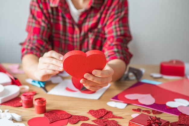 Zdjęcie kartka świąteczna diy z czerwonym papierowym sercem, symbolem miłości. dziewczyna sprawia, że dzień matki, walentynki, kartkę z życzeniami. hobby, koncepcja sztuki, prezent własnymi rękami