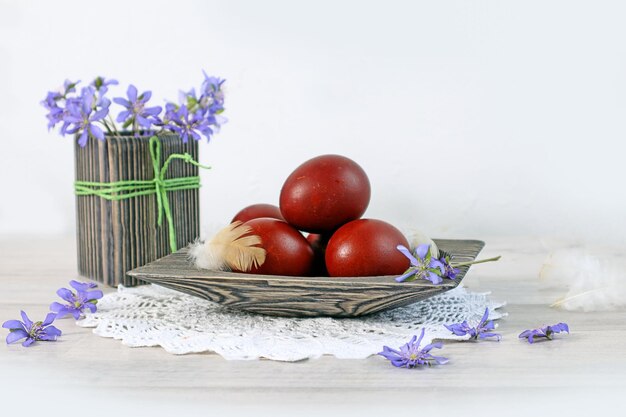 Kartka wielkanocna malowane jajka w drewnianej misce bukiet wiosennych kwiatów w wazonie na białej koronkowej serwetce jasne tło miejsce na tekst
