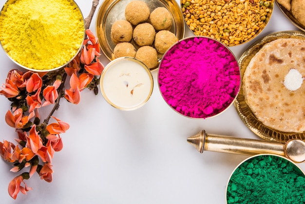 Kartka z życzeniami Happy Holi przedstawiająca tradycyjne indyjskie słodkie i słone potrawy, kwiaty i kolory proszku ułożone na białym tle lub glinie. Selektywne skupienie